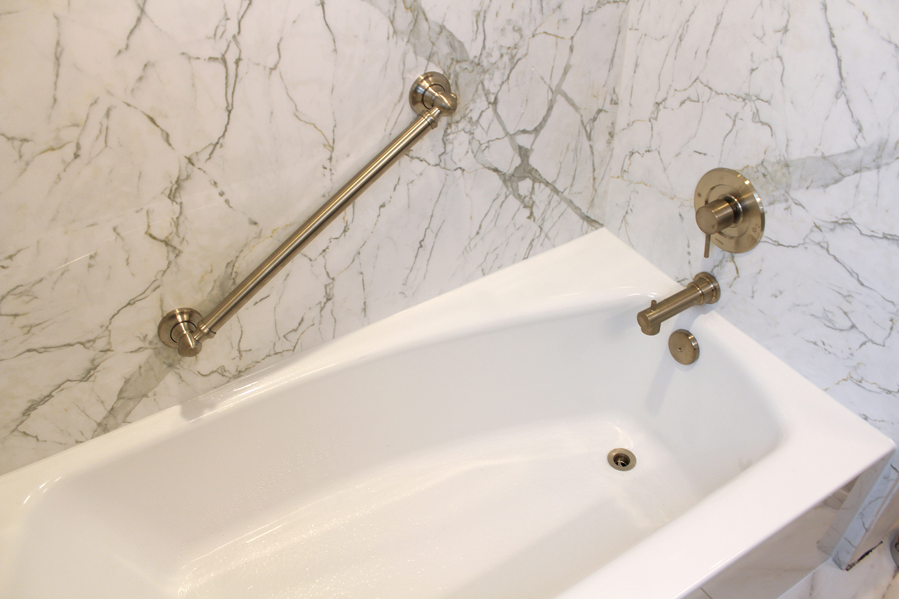Brushed gold grab bar and faucet detail on Calcutta marble wall surround